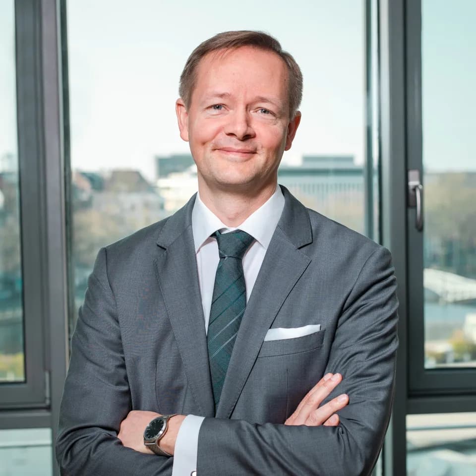 Porträt von Dr. Lars Holldorf im grauen Anzug vor einem Bürofenster